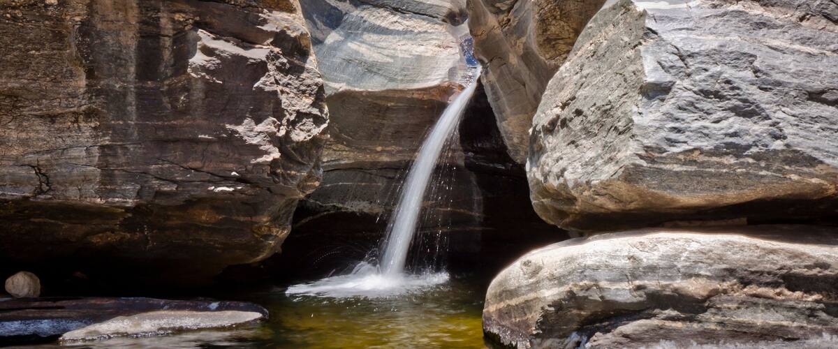 A waterfall cascading down a rocky gorge with large boulders surrounding the water.