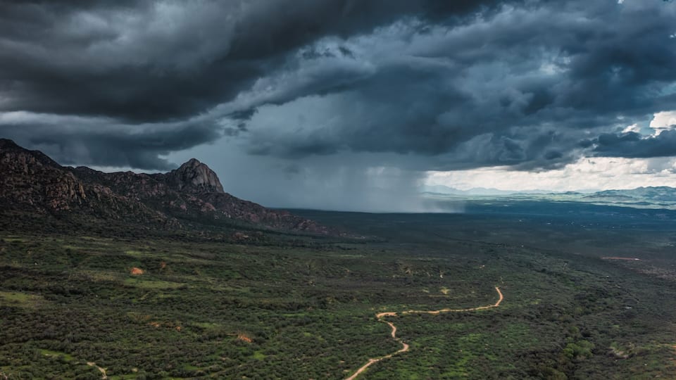 A mountainous landscape with a winding road and a stormy sky.