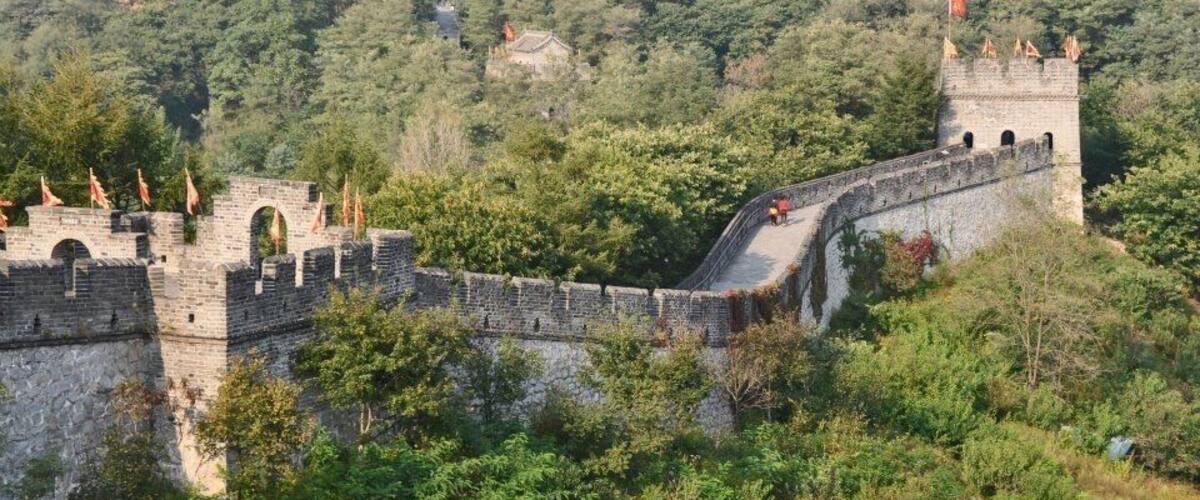 The Great Wall of China winding through a lush, green landscape with stone towers and watchtowers.