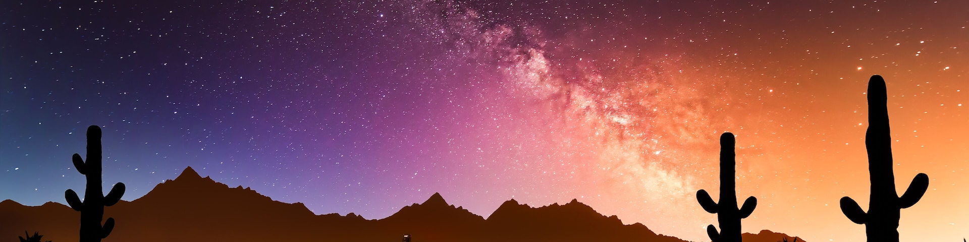 A night sky with stars and the Milky Way over a cityscape with mountains in the background.
