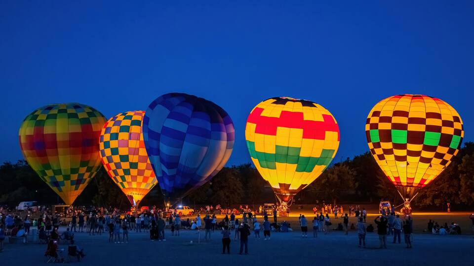 A nighttime hot air balloon festival with colorful balloons and a crowd of spectators.