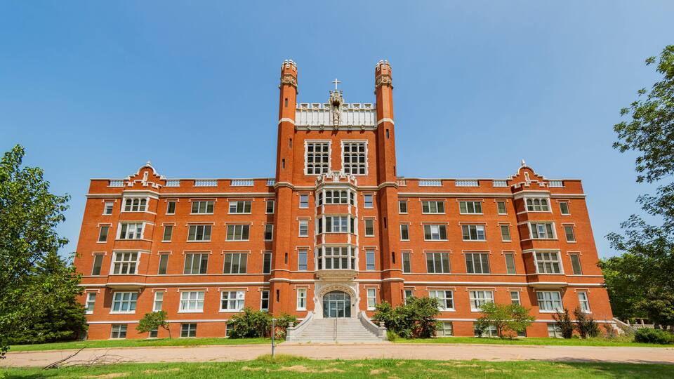 A large red brick building with a central tower, large windows, and a staircase leading to the entrance.