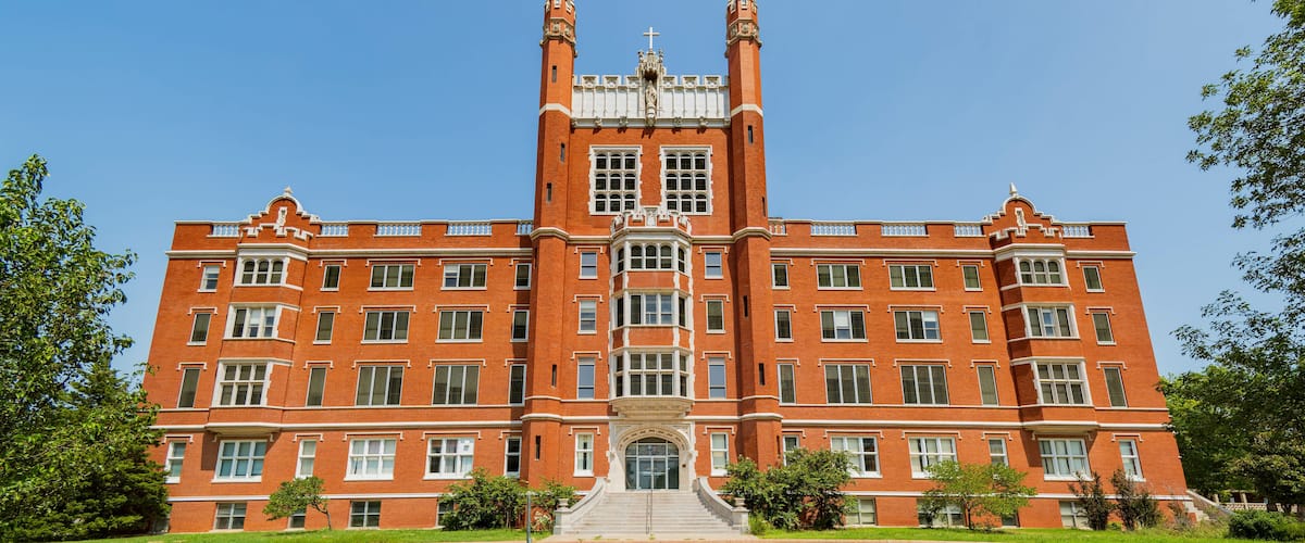 A large red brick building with a central tower, large windows, and a staircase leading to the entrance.