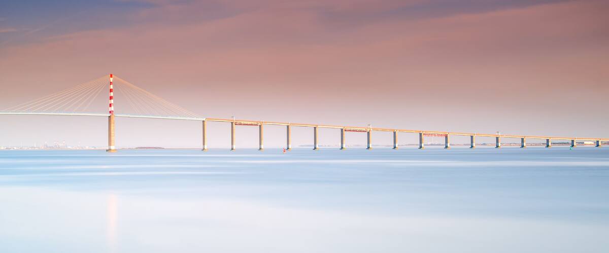 A long suspension bridge over calm water with a clear sky.