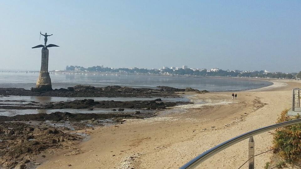A coastal view with a rocky shoreline, a sandy beach, and a statue on a pillar.