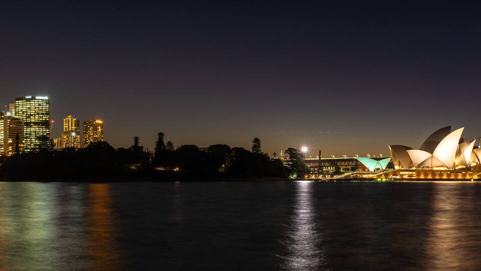 A city skyline with illuminated buildings, a bridge, and the Sydney Opera House.