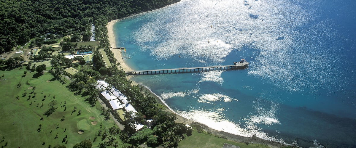 A coastal landscape with a pier extending into the sea, surrounded by lush greenery and a clear sky.