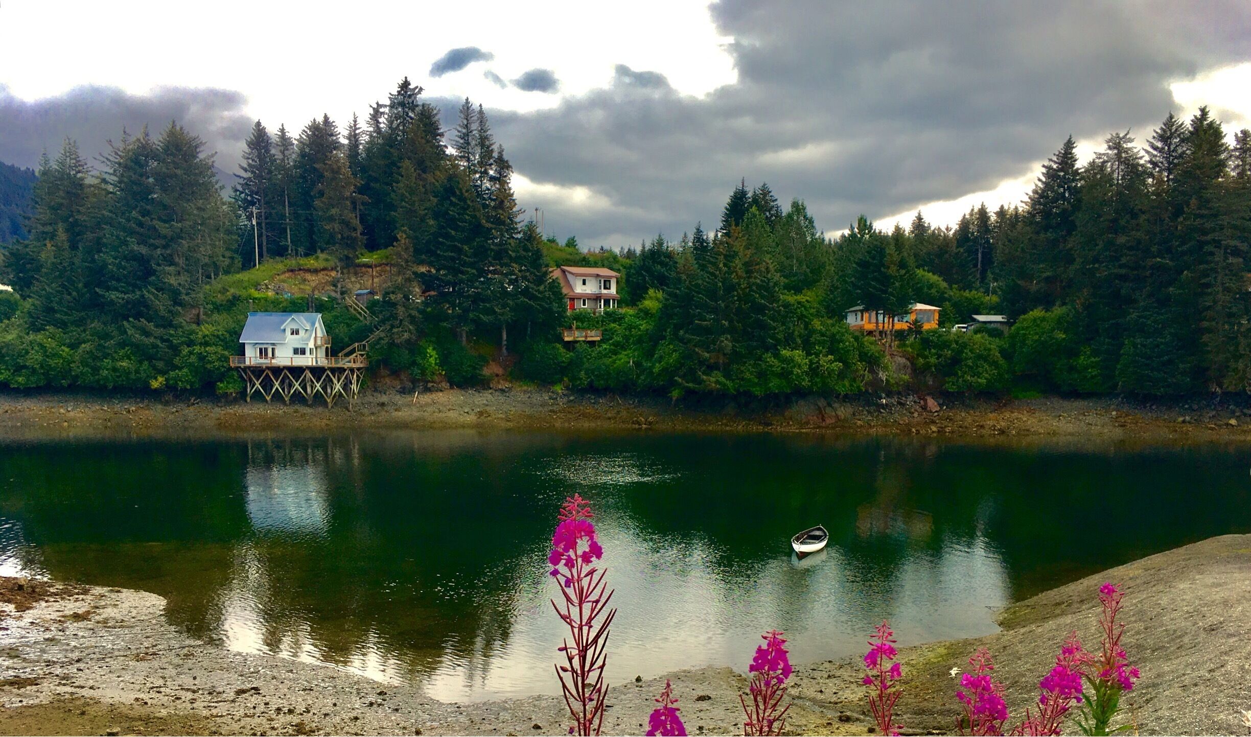 A lake with houses on stilts, surrounded by dense forest and a cloudy sky.