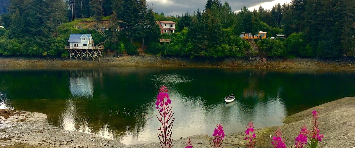 A lake with houses on stilts, surrounded by dense forest and a cloudy sky.