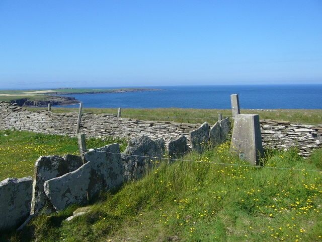 A stone wall with a view of the sea and distant land.