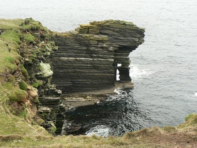 A coastal rock formation with layered strata and a small inlet.