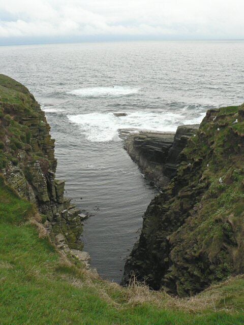 A coastal cliff with a narrow waterway between two steep rock faces.
