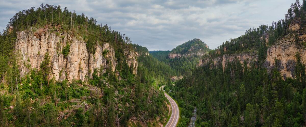 A winding road through a forested valley with rocky cliffs.
