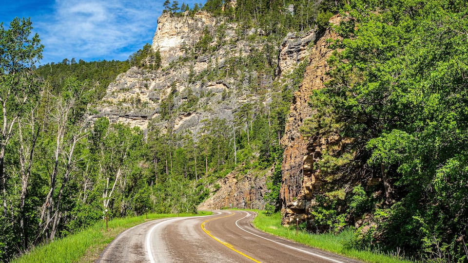 A winding road through a forested area with a rocky cliff on the right.
