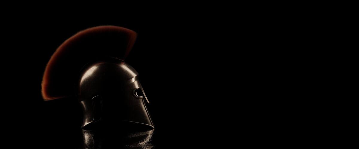 A helmet with a red plume against a dark background.