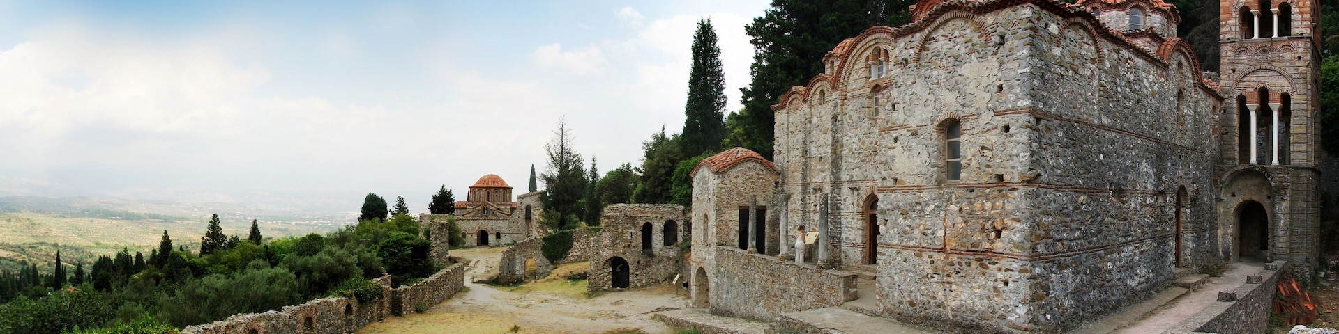 An ancient stone church with a red-tiled roof, surrounded by ruins and greenery.