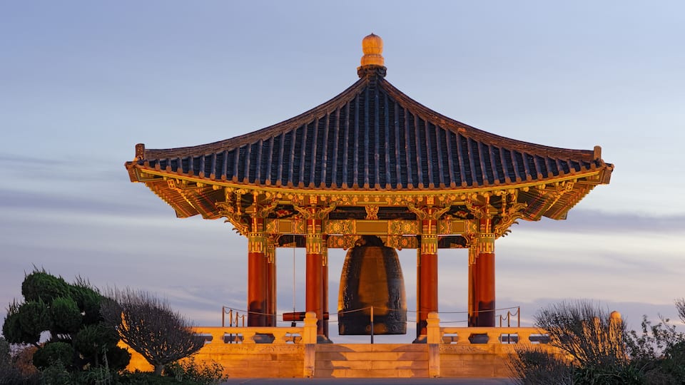A traditional pavilion with a curved roof and ornate decorations, set against a twilight sky.