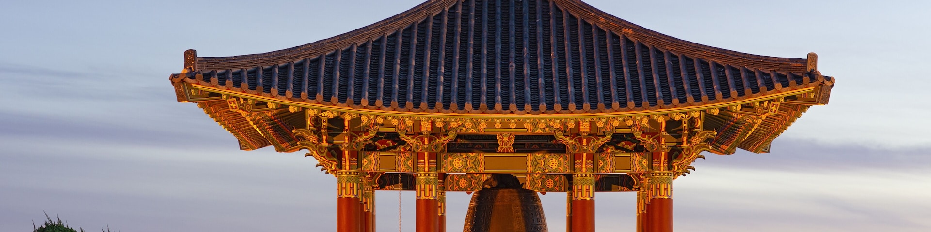 Un pabellón tradicional con techo curvo y decoraciones ornamentales, al atardecer.