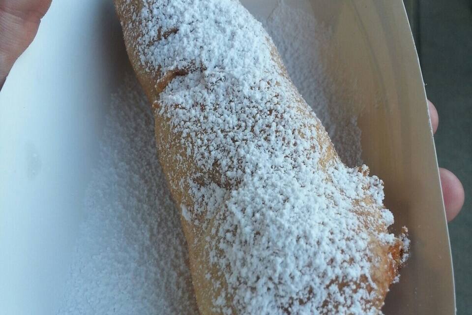 A hand holding a powdered pastry in a paper container.