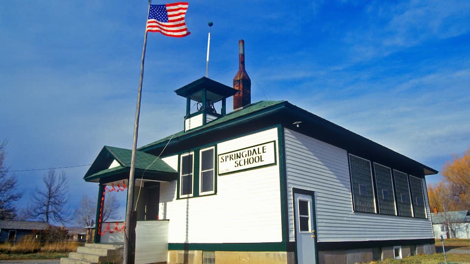 A white school building with a green roof, labeled "Springdale School," and an American flag flying atop.