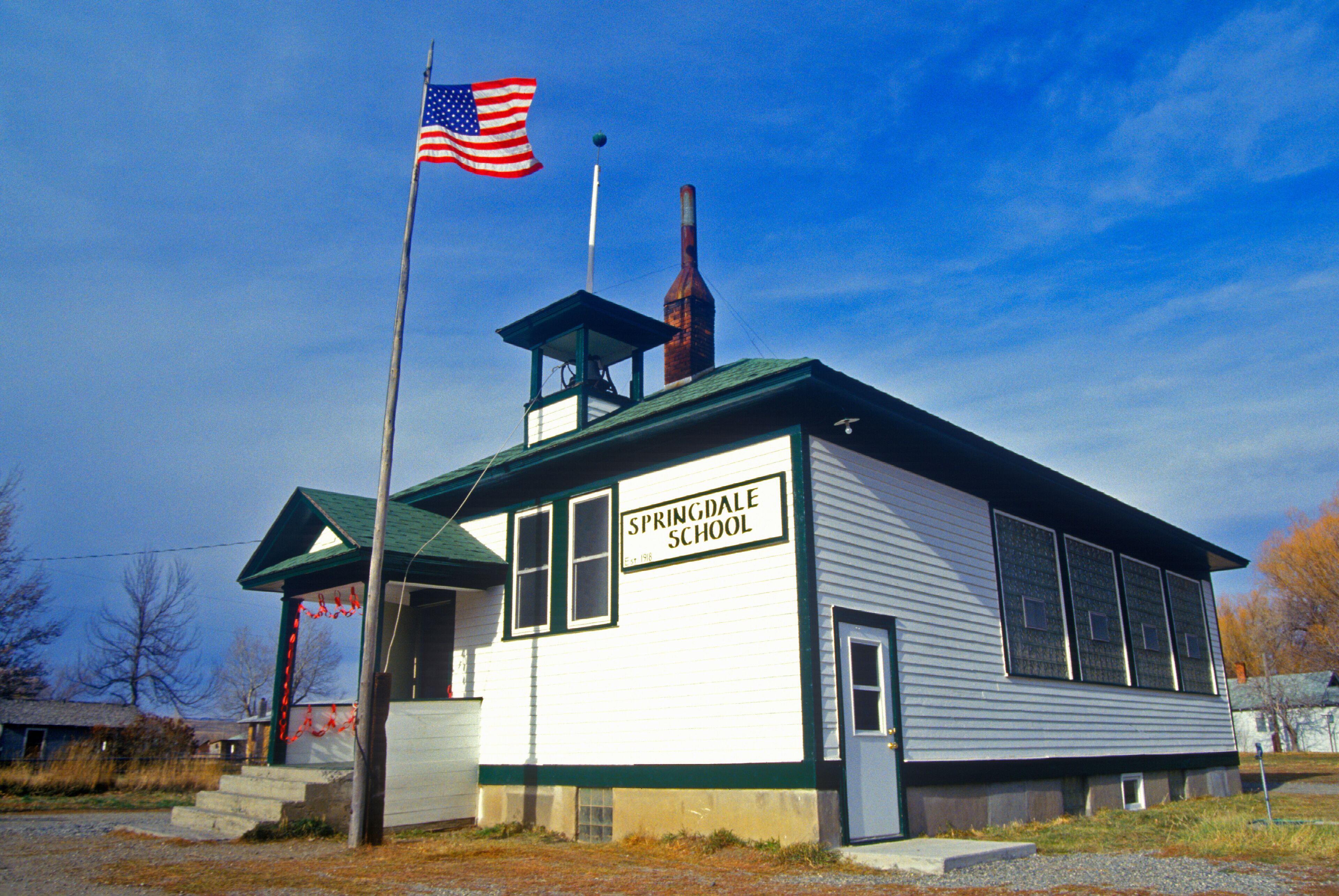 A white school building with a green roof, labeled "Springdale School," and an American flag flying atop.