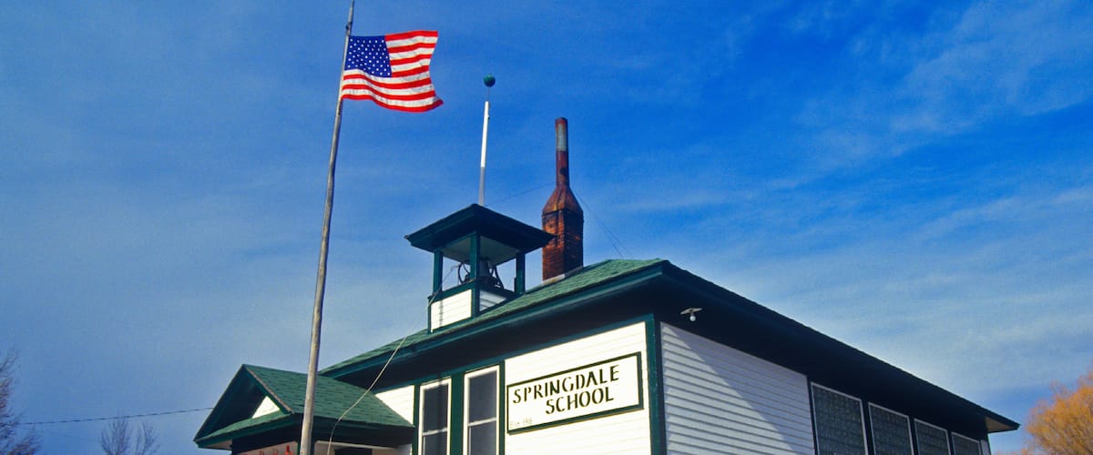 A white school building with a green roof, labeled "Springdale School," and an American flag flying atop.