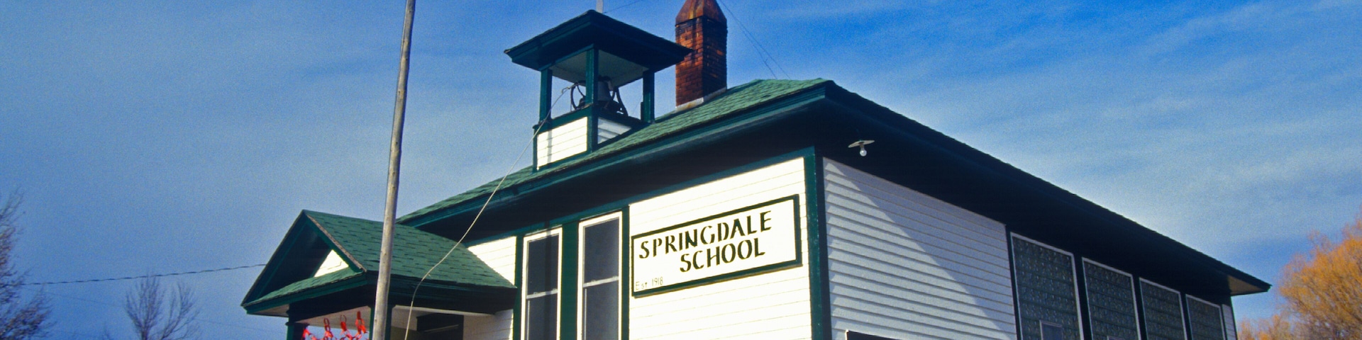 A white school building with a green roof, labeled "Springdale School," and an American flag flying atop.