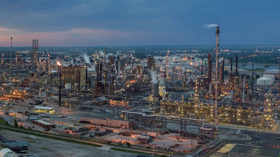 An industrial complex with multiple large buildings and storage tanks near a body of water.