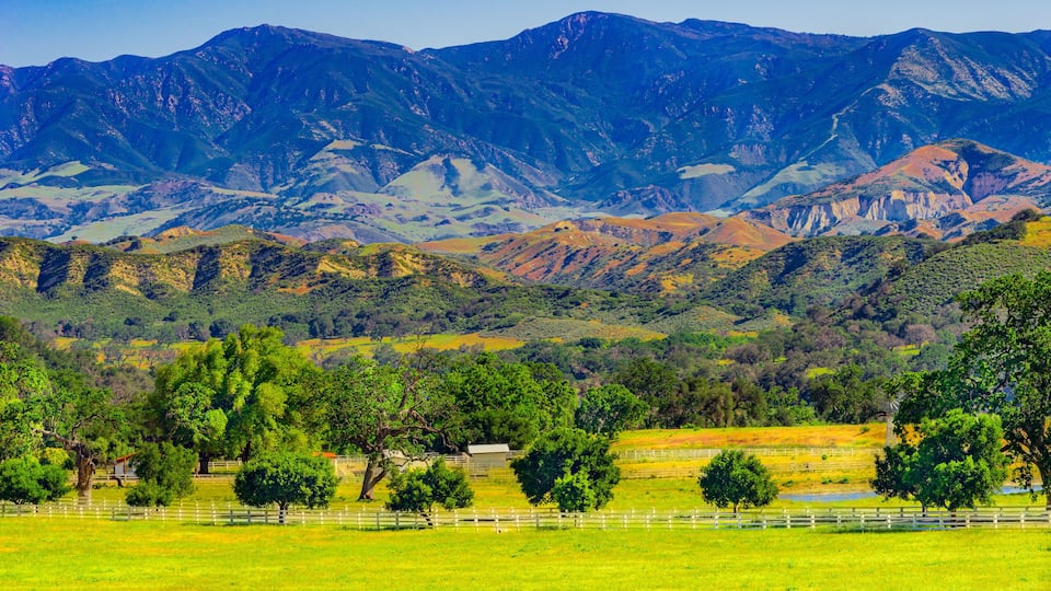 A mountainous landscape with green fields and trees in the foreground.