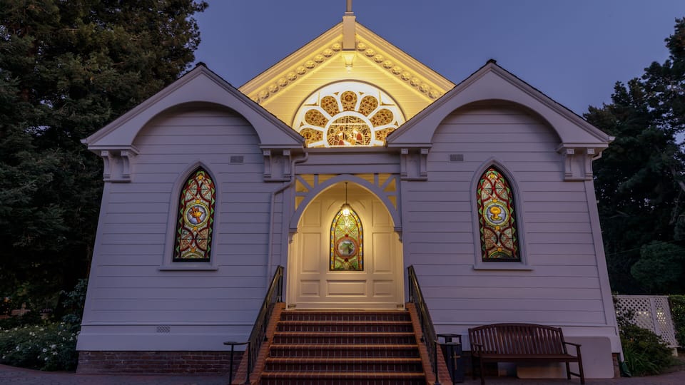 A church with a cross on the roof, stained glass windows, and a bench in front.