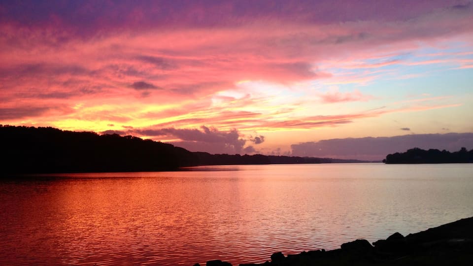 A sunset over a calm lake with silhouetted hills in the background.