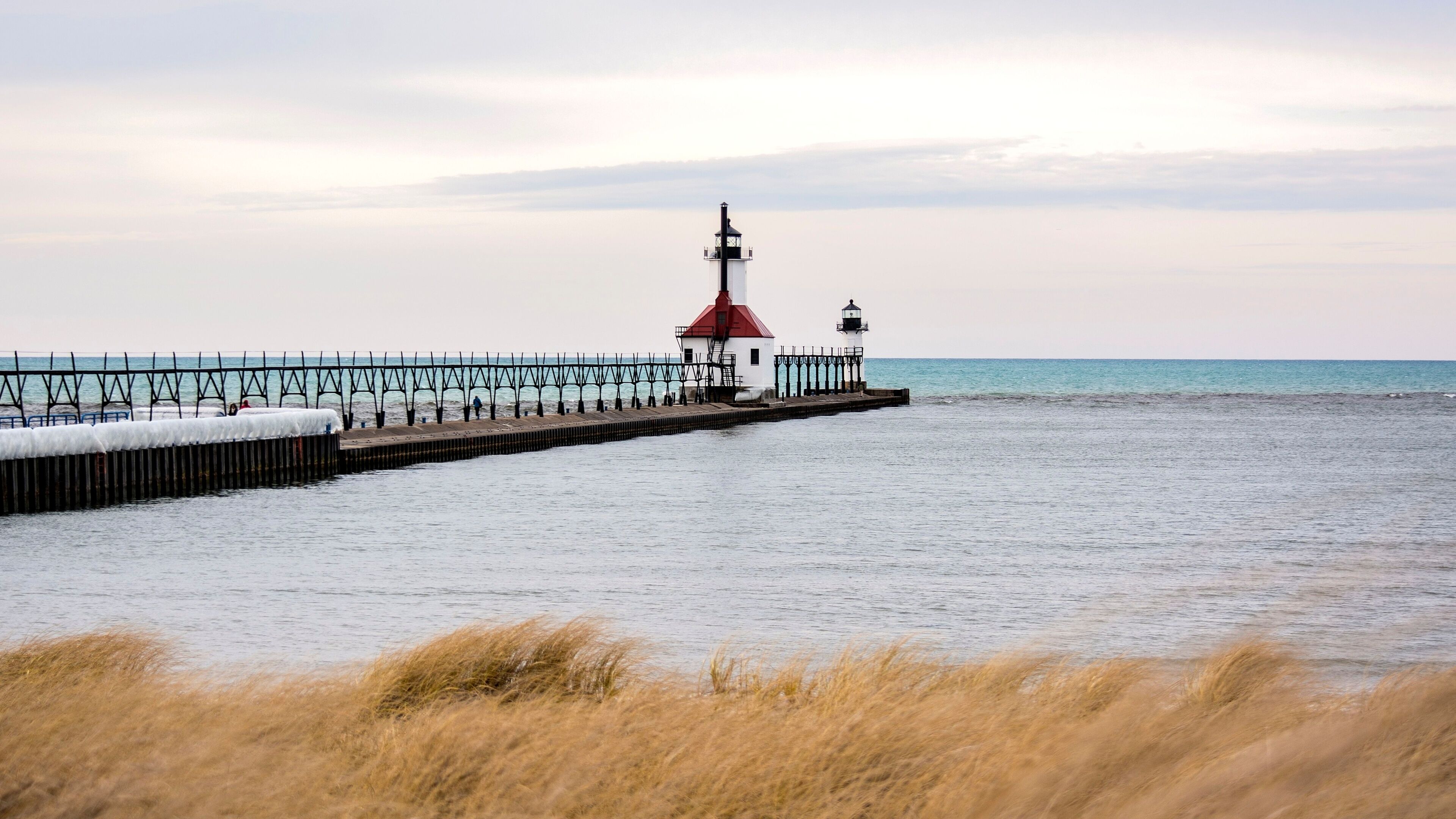 A lighthouse on a pier extending into calm waters, with a clear sky above.