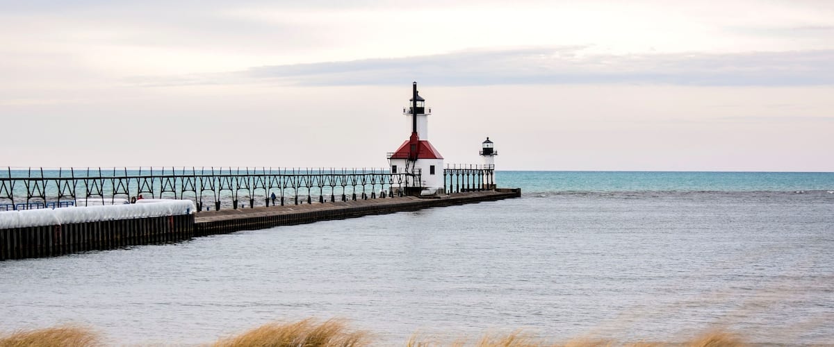A lighthouse on a pier extending into calm waters, with a clear sky above.