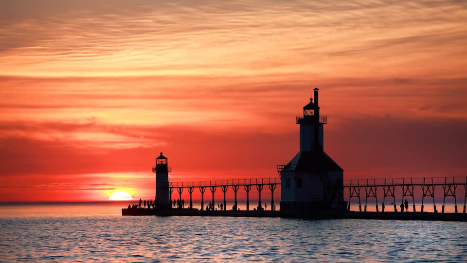 A lighthouse at sunset with a pier extending into the water.