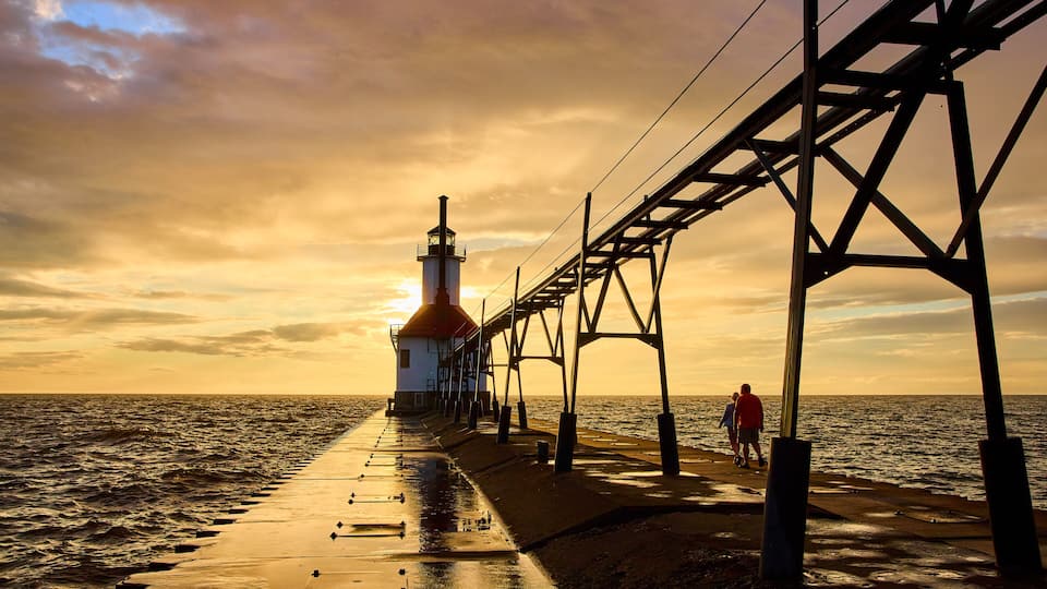 A pier extending into the sea with a lighthouse at the end, under a sunset sky.