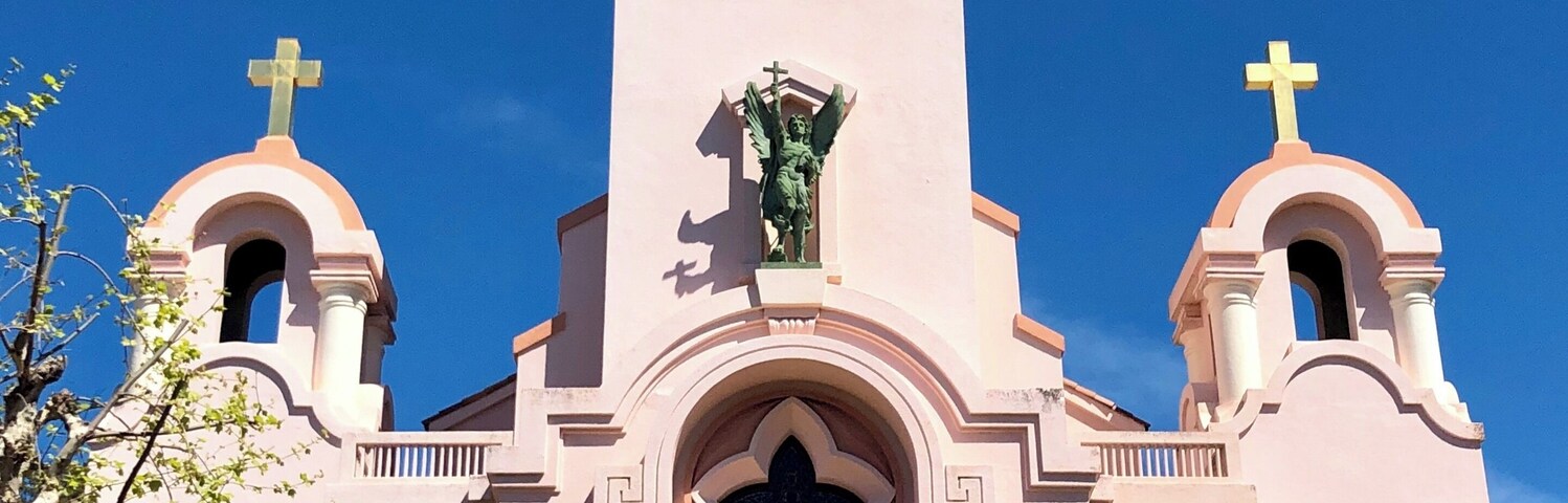 Una iglesia rosa con una torre central, dos torres laterales y una gran cruz en la parte superior.