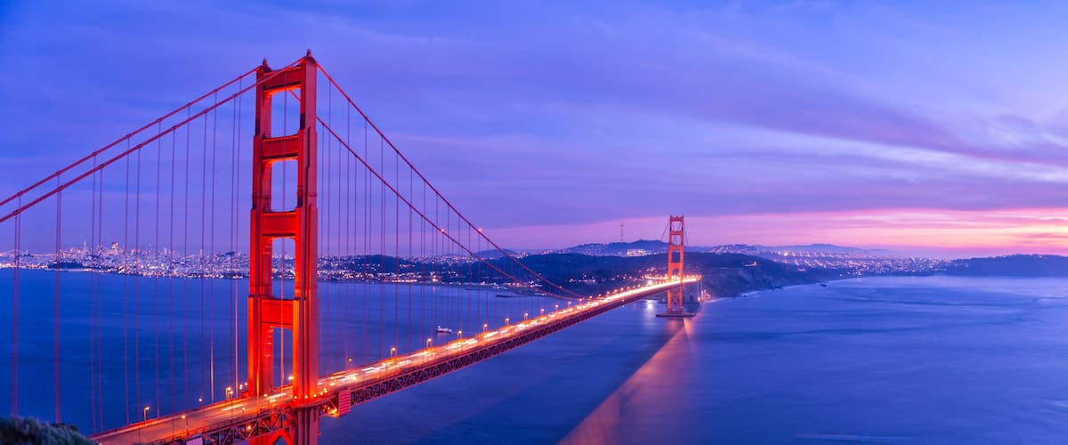 The Golden Gate Bridge at dusk with city lights in the background.