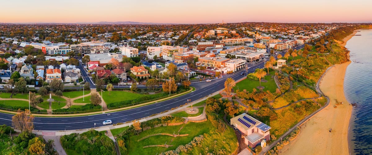 An aerial view of a coastal town with a beach, roads, and residential buildings.