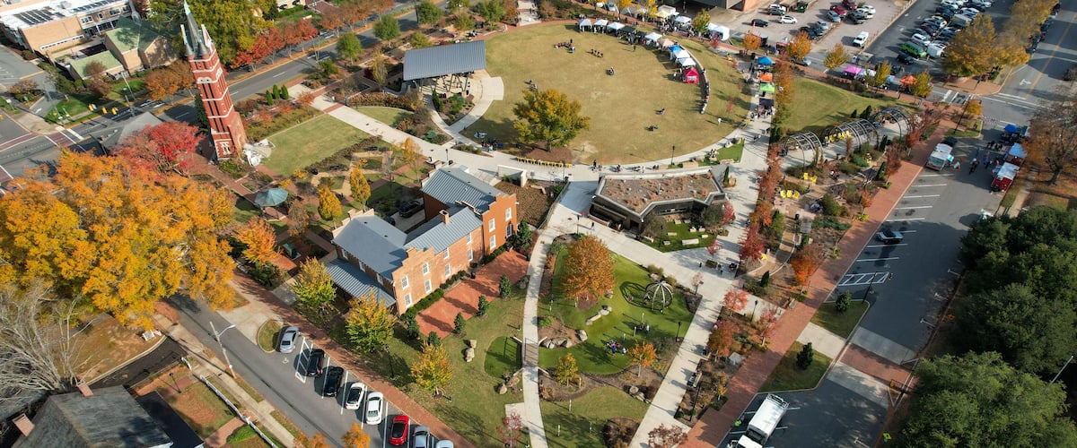 Luchtbeeld van een universiteitscampus met een centraal gazon, omliggende gebouwen en een parkeerplaats.