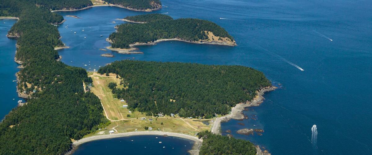 An aerial view of a coastal area with multiple islands, clear blue waters, and a few boats.