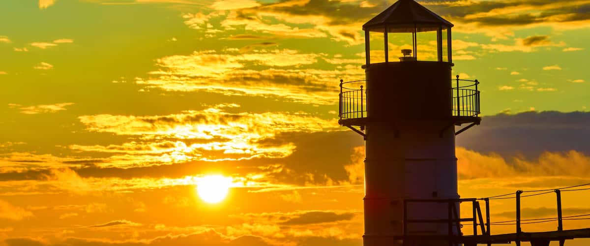 A lighthouse silhouette against a sunset sky.