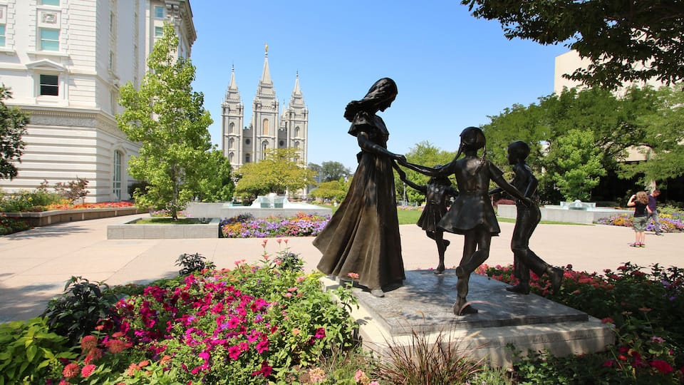 A statue of a woman and two children in a garden with a cathedral in the background.