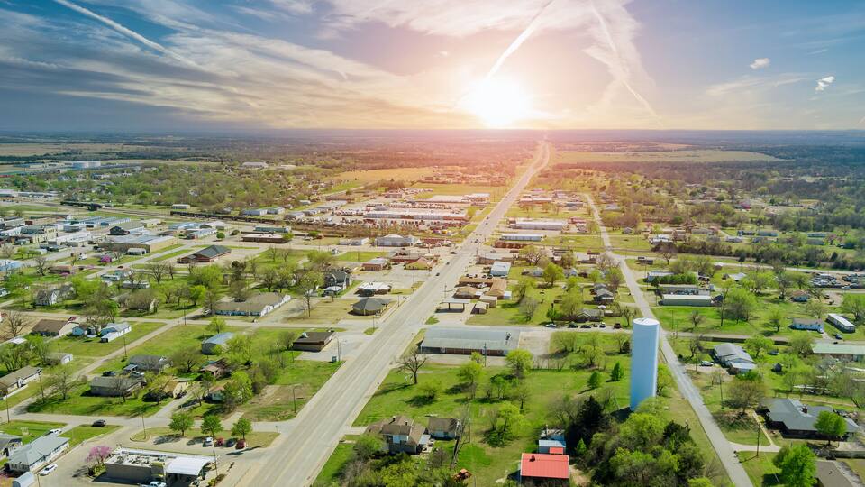 An aerial view of a suburban area with a prominent blue water tower, a main road, and scattered residential houses.