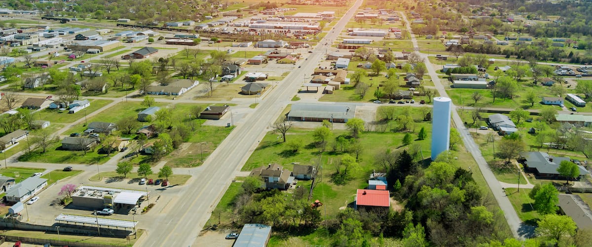 An aerial view of a suburban area with a prominent blue water tower, a main road, and scattered residential houses.