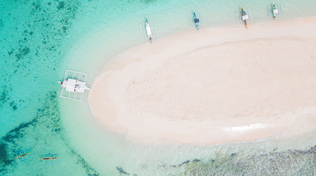 An aerial view of a beach with clear turquoise waters, a sandy shore, and several small boats anchored near the water's edge.