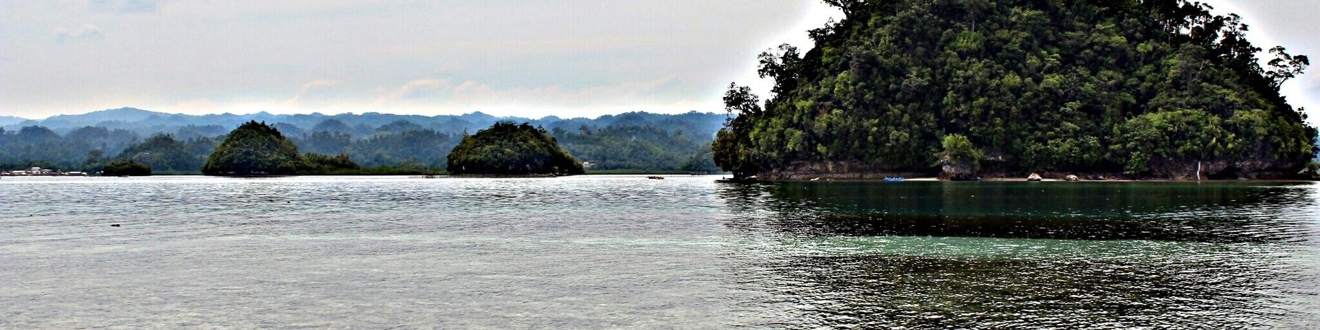 Un lago tranquilo con aguas cristalinas, rodeado por una orilla arenosa y varias islas pequeñas cubiertas de vegetación densa.