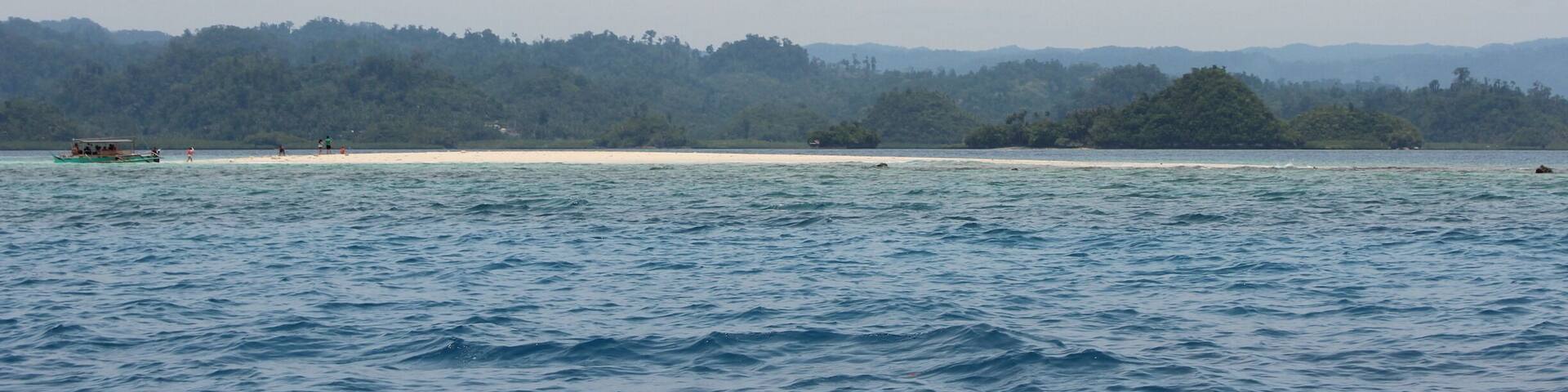 A calm sea with a boat and a sandy beach in the distance.