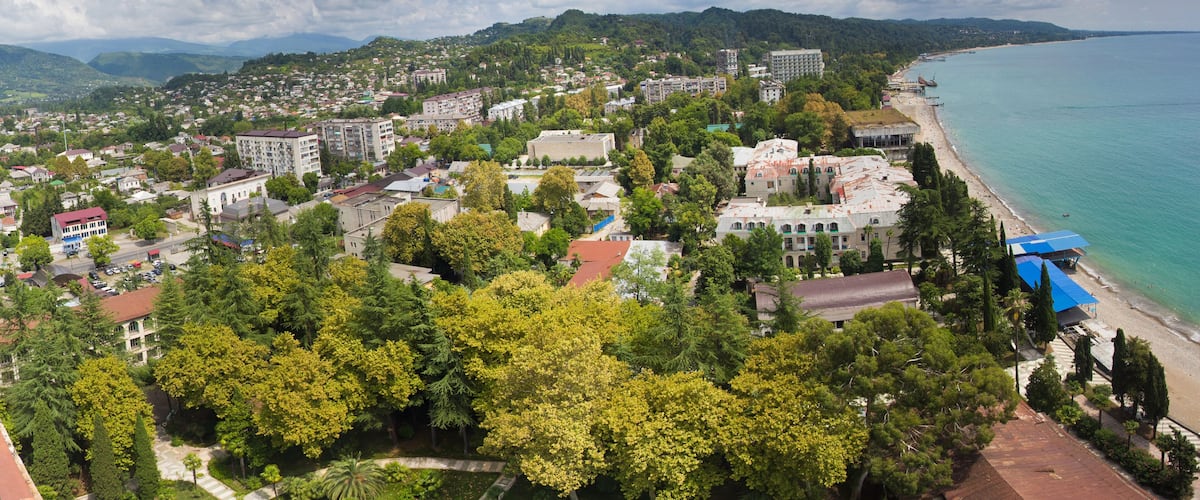 A coastal town with a beach, dense greenery, and a mountainous backdrop.