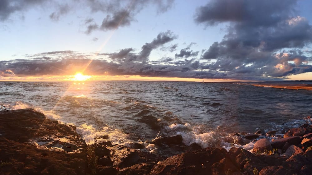 A sunset over a rocky coastline with waves crashing against the shore.
