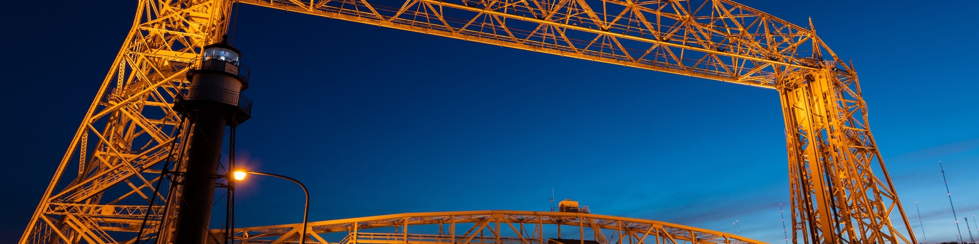 A large steel bridge structure at night with lights reflecting on the water.